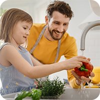Vater und Tochter waschen gemeinsam eine Paprika unter fließendem Wasser in der Küche – bewusstes Einkaufen und gesunde Ernährung für Kinder im Familienalltag durch Ernährungsberatung für Kinder.