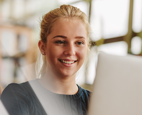 Junge Frau nimmt lächelnd an einer Online-Infoveranstaltung der EHiP teil, sitzt mit Laptop und Headset in modernem, hellen Raum.