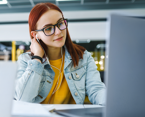 Junge Frau nimmt lächelnd an einer Online-Infoveranstaltung der EHiP teil, sitzt mit Laptop und Headset in modernem, hellen Raum.