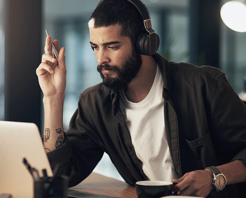 Mann nimmt an einer Online-Infoveranstaltung teil, sitzt mit Laptop, Headset und Notizbuch in modernem, hellen Raum.